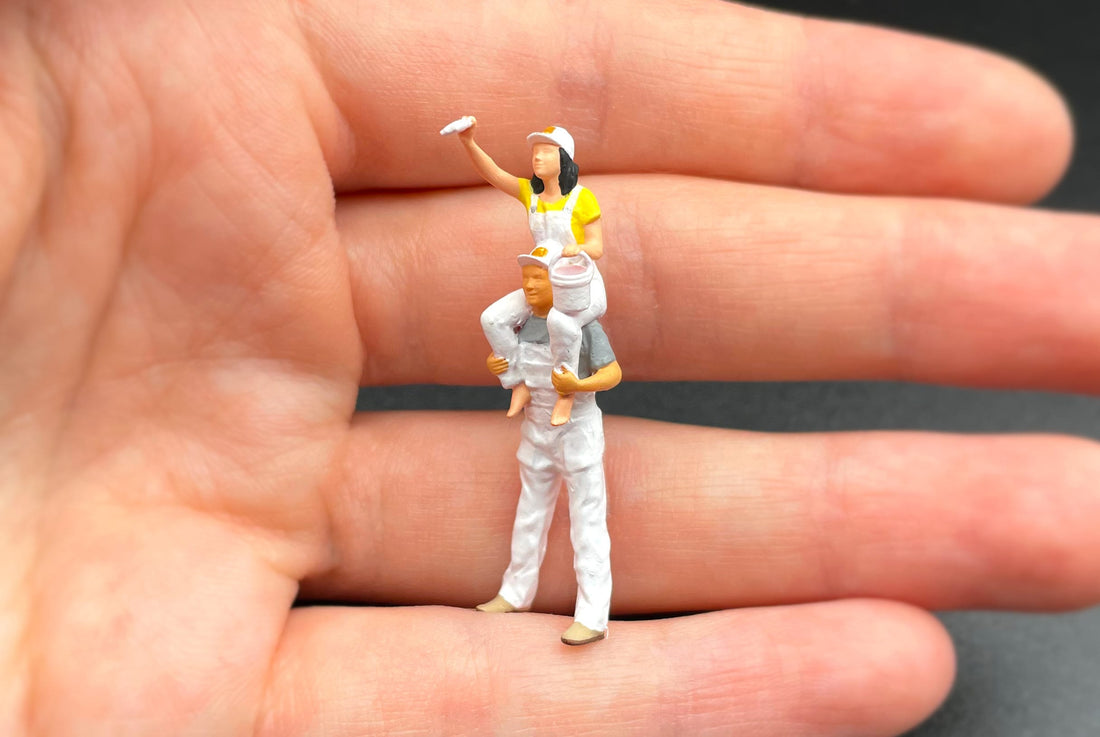 Hand-painted 1:64 scale painter figures standing on the palm of a hand, showing how small they are
